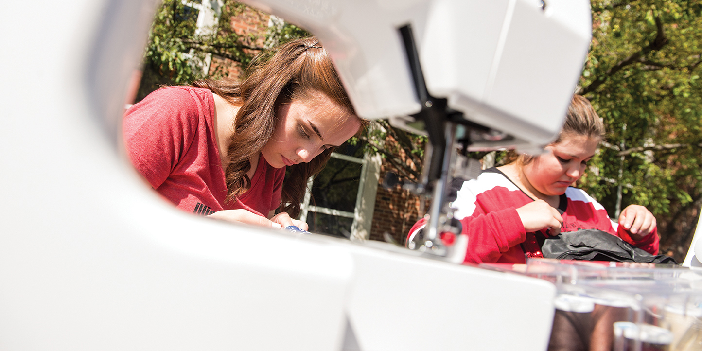 两名家庭和消费者科学专业的学生在“周五修理”活动中使用缝纫机。