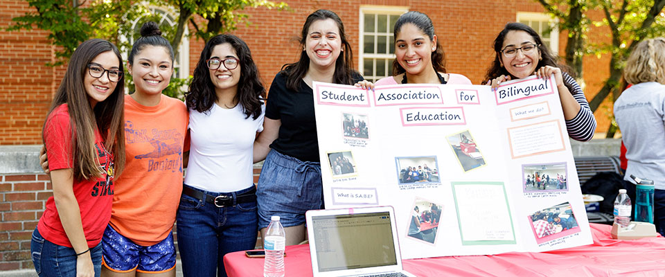 在ISU节日期间，几名大学生在双语教育学生协会的桌子上对着镜头摆姿势。