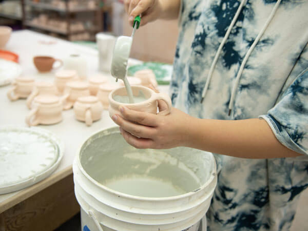 一名学生将釉料倒入他们的陶瓷马克杯。