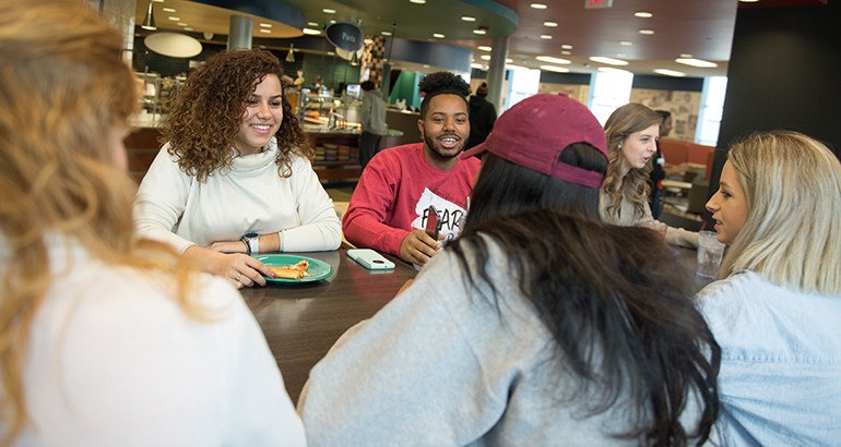 一群学生在沃特森餐饮中心的一张桌子边聊天边吃饭。