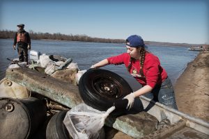伊利诺斯州学生凯特林Remian加载一个废弃轮胎到一艘船在密西西比河的清理另一个优惠格拉夫顿之旅,伊利诺斯州。