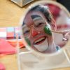 乔恩·富尔顿在镜子里的倒影。富尔顿化着小丑妆，用化妆刷在脸颊上画了一个绿色的圈。