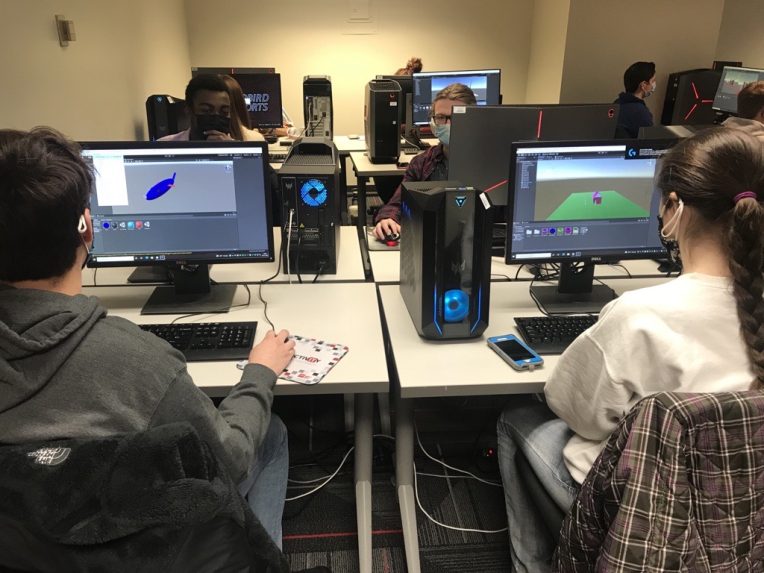 一群蒙面学生坐在电脑丛朱利安·霍尔在他们的虚拟现实(VR)项目在电脑上