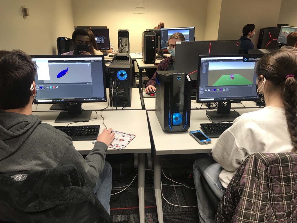 一群戴着面具的学生坐在朱利安大厅的计算机群前，在他们的电脑上进行虚拟现实(VR)项目