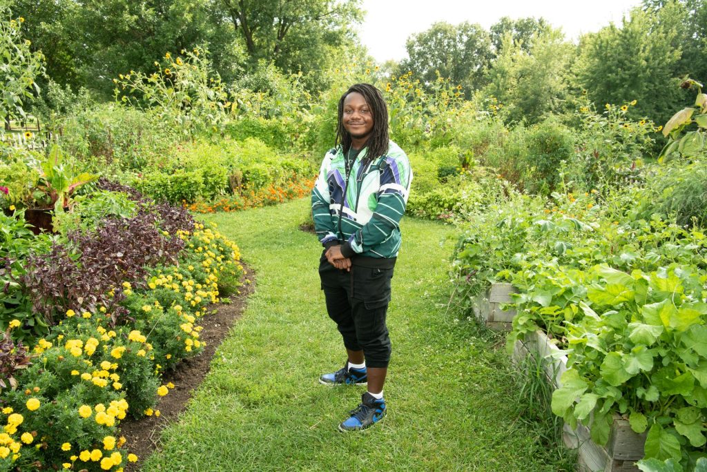 学生戴着五彩缤纷,绿色夹克站在一个花园