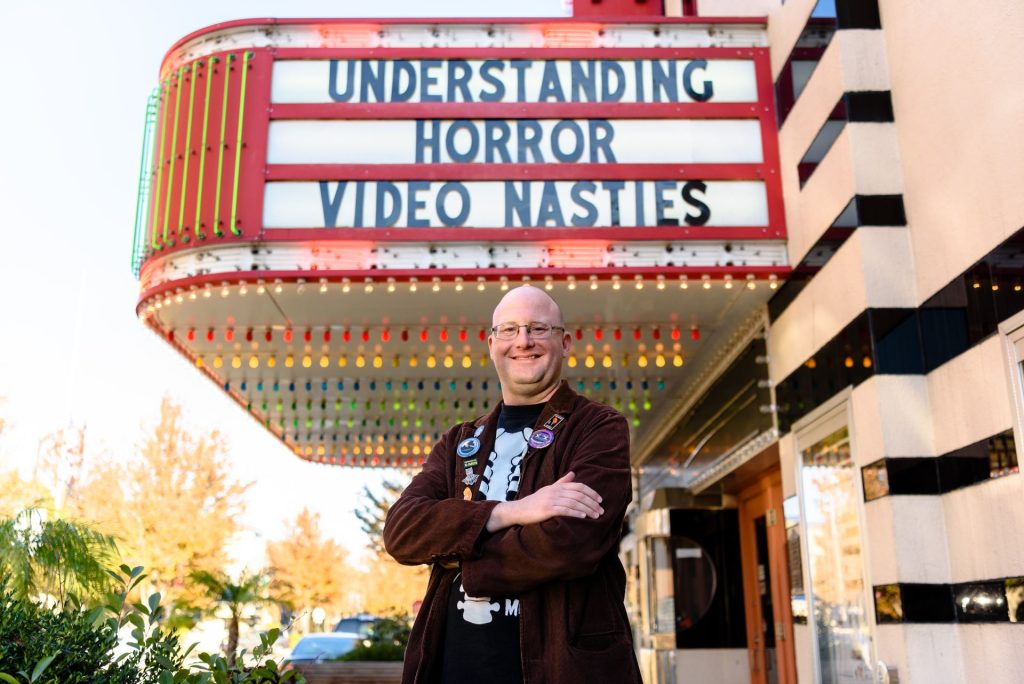 埃里克·韦塞尔曼博士在普通剧院的大招牌前摆姿势，上面写着“理解恐怖:肮脏的视频”。