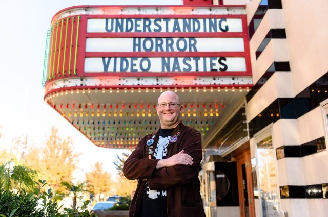 埃里克·韦塞尔曼博士在普通剧院的大招牌前摆姿势，上面写着“理解恐怖:肮脏的视频”。