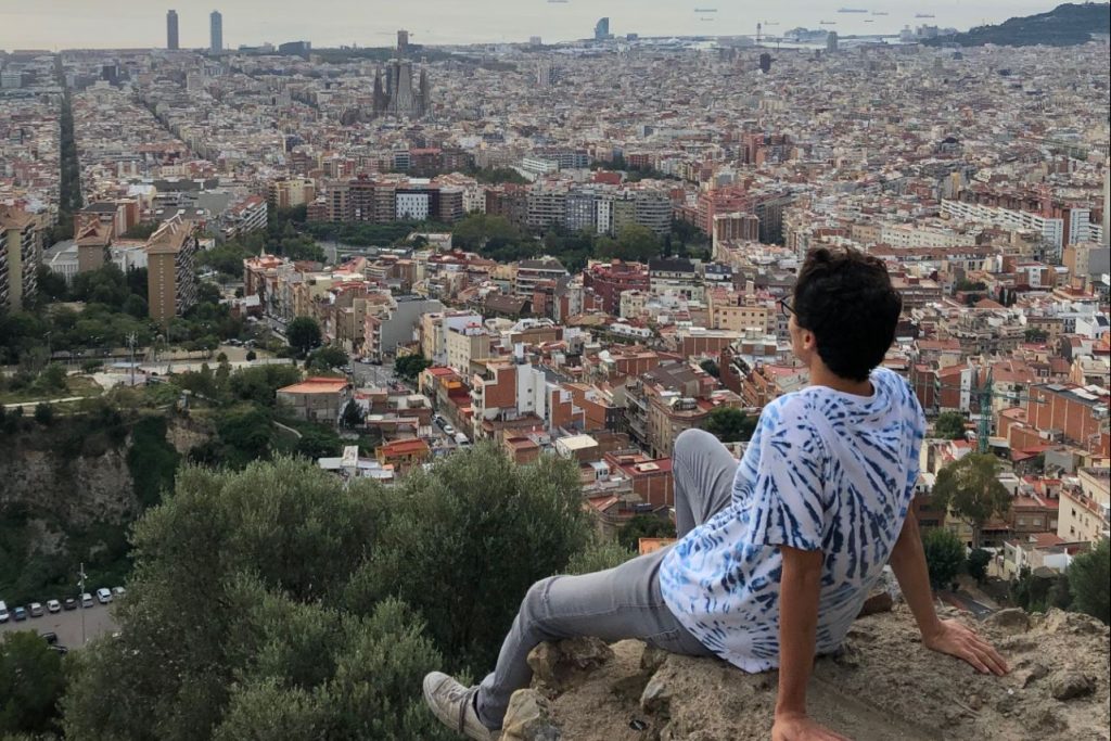 学生坐在岩壁上，远眺古老的意大利城市。