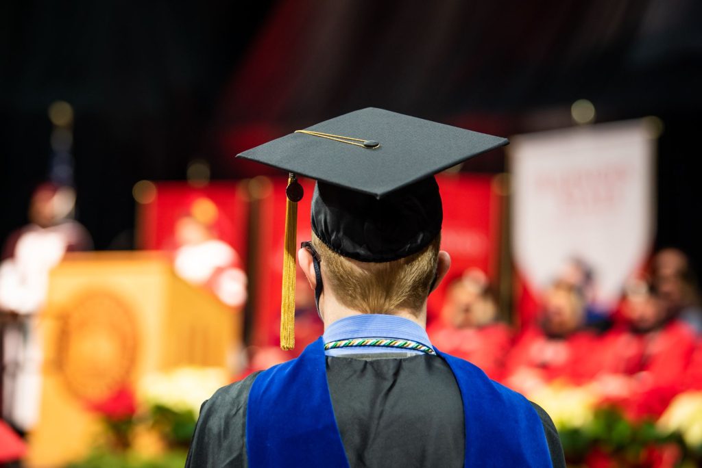 一个学生的后脑勺，戴着学士帽，后面是毕业典礼的舞台