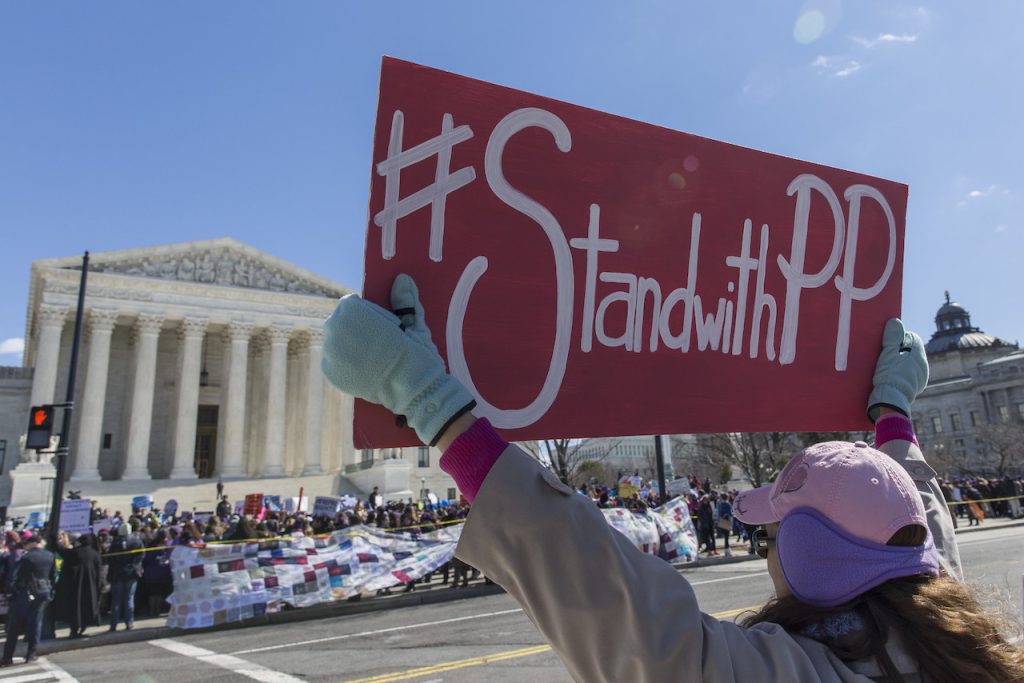 一个人拿着一个粉红色的“# StandwithPP”标志在美国最高法院面前