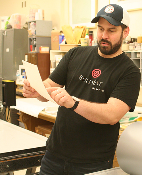 艺术家马修·戴·佩雷斯(Matthew Day Perez)站在工作室里，指着手中的一张纸。