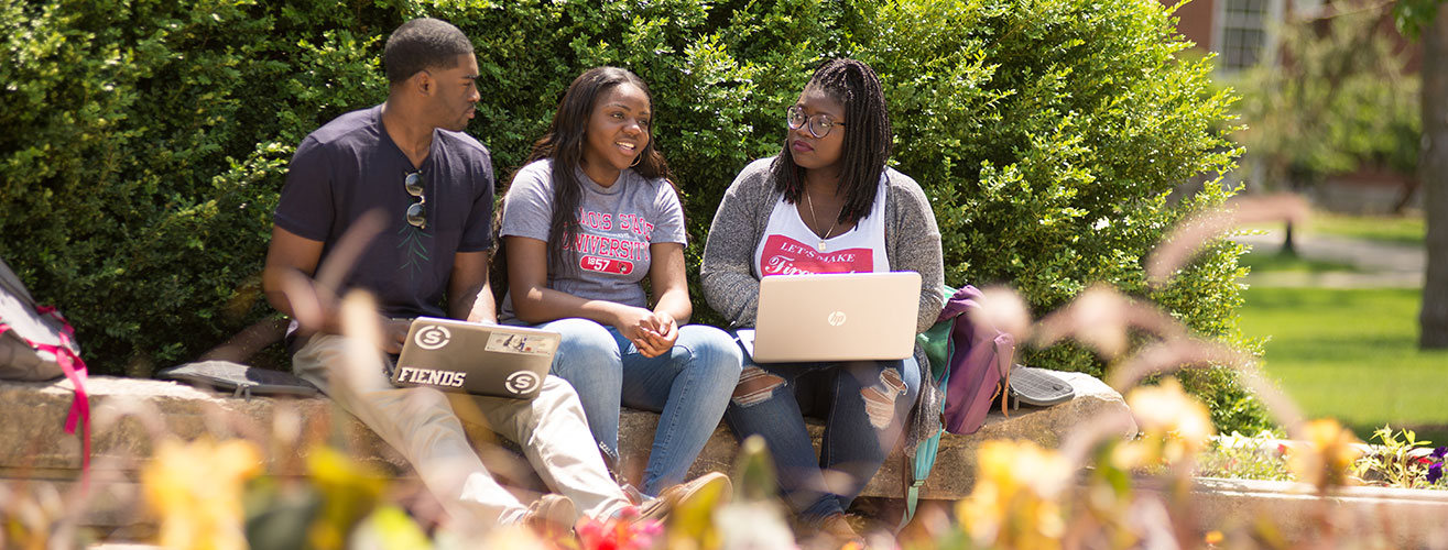 3名非裔美国学生坐在外面玩电脑