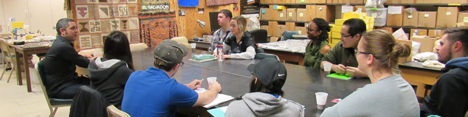 一个人类学小班学生围坐在一张桌子旁，聚精会神地听着教授讲课。