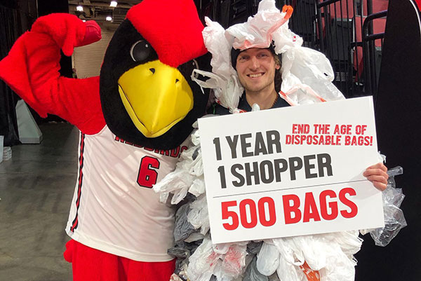 一名学生和戴着塑料袋的雷吉合影，并举着“一年，一个购物者，500个袋子”的牌子。