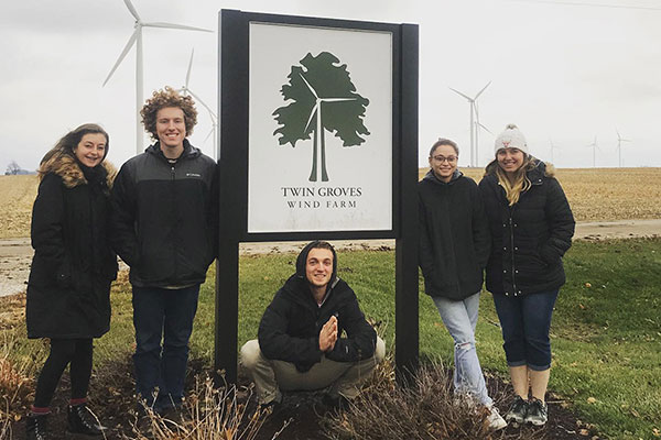 五个学生站在双子格罗夫斯风电场的标志周围。