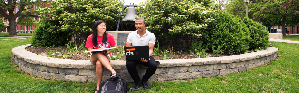 两个学生拿着笔记本电脑坐在院子里。