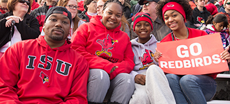 一家人穿着ISU装备坐在看台上看足球比赛，牌子上写着“红鸟加油”